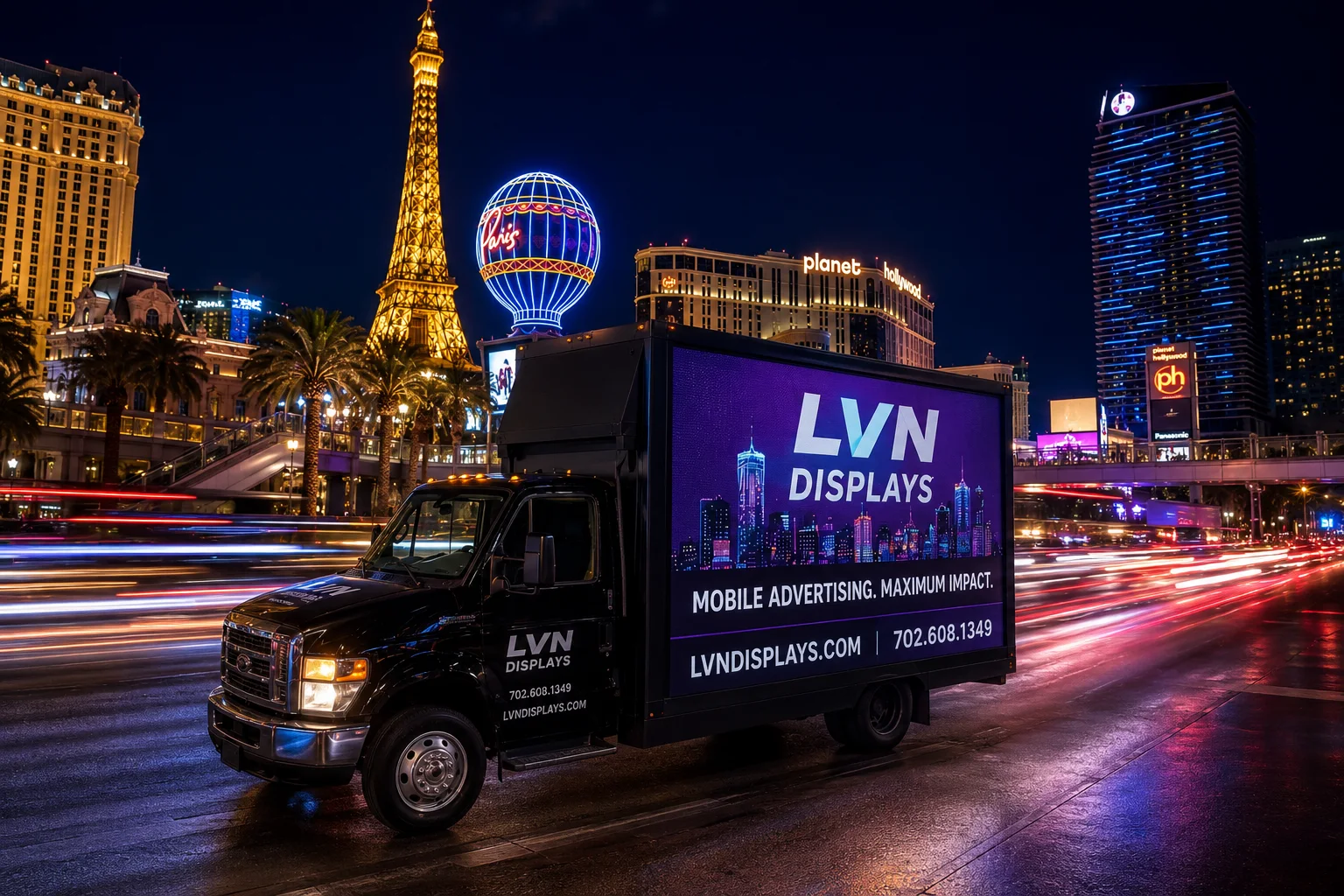 LVN Displays black box truck with a full-color side LED screen advertising on the Las Vegas Strip at night, Paris balloon and Planet Hollywood behind, blurred traffic light trails