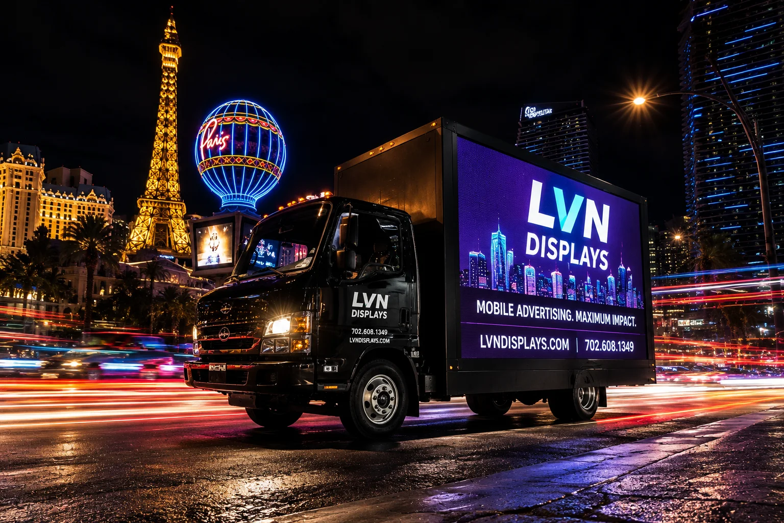 LVN Displays LED billboard box truck on the Las Vegas Strip at night, headlights on, Eiffel Tower and Paris balloon behind with streaking car light trails