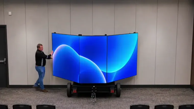An LV Displays fold-out trailer fully deployed into a three-panel panoramic LED display with an operator alongside for scale